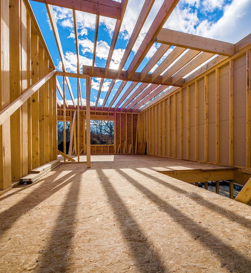Wooden house frame under construction, sunny day.