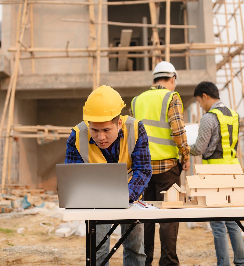 Construction workers using laptop at building site.
